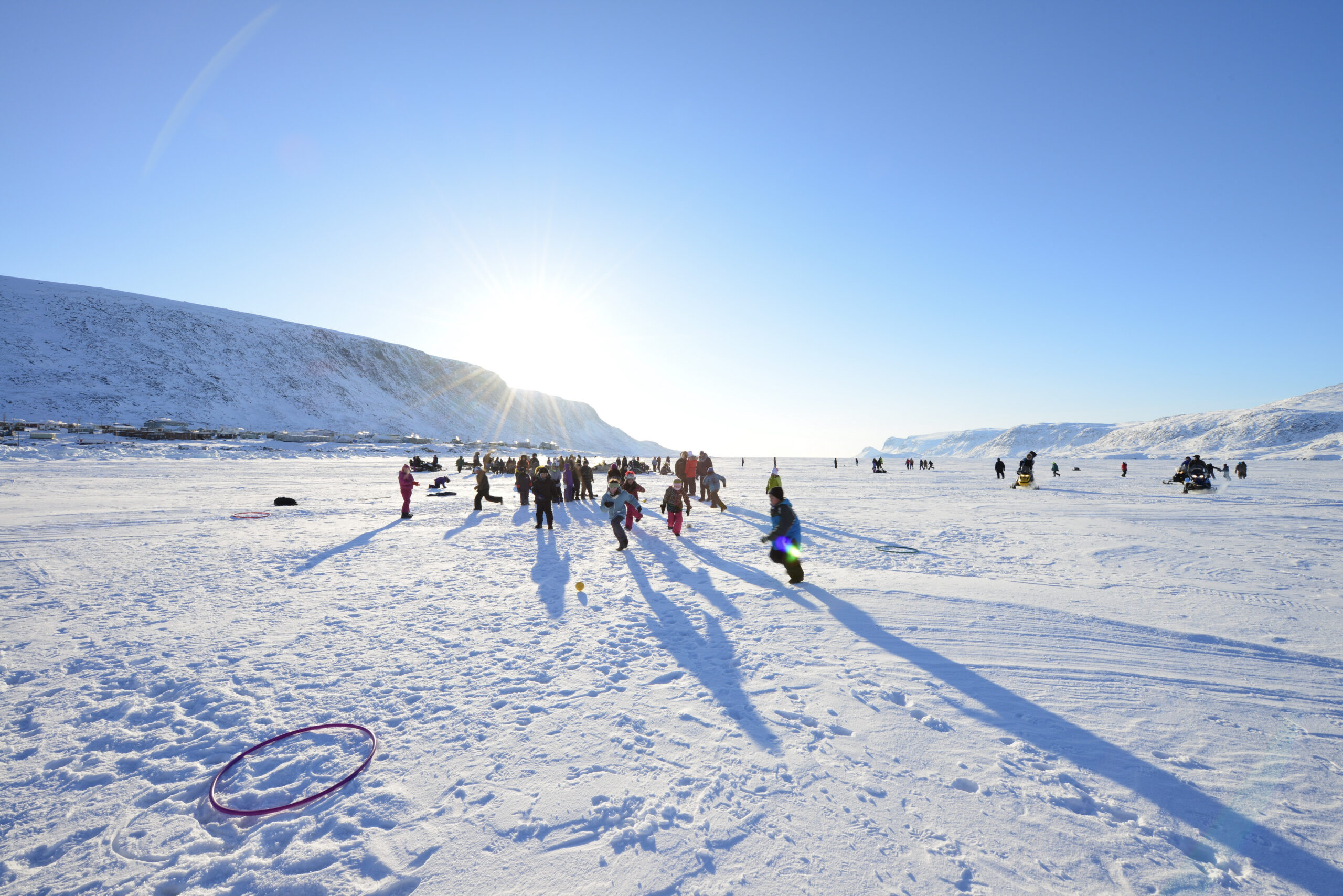Indigenous youth playing outside in the snow with a bright sun in the background.