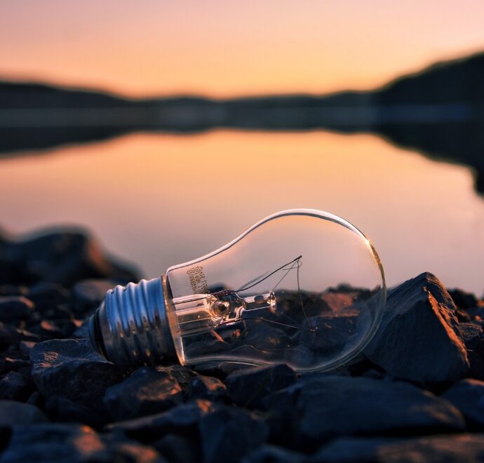 Lightbulb on top of rocks next to a lake at sunset