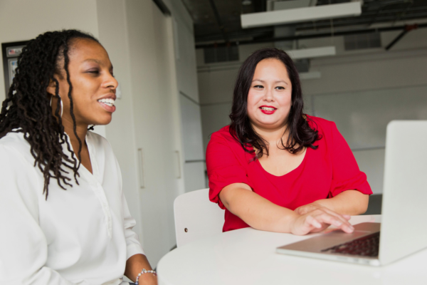 Two individuals sitting at a white table with a laptop, engaged in a conversation about student placement opportunities at Kids Help Phone.