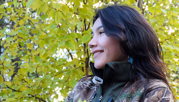 Photo of smiling young person in front of a tree with yellow and green leaves