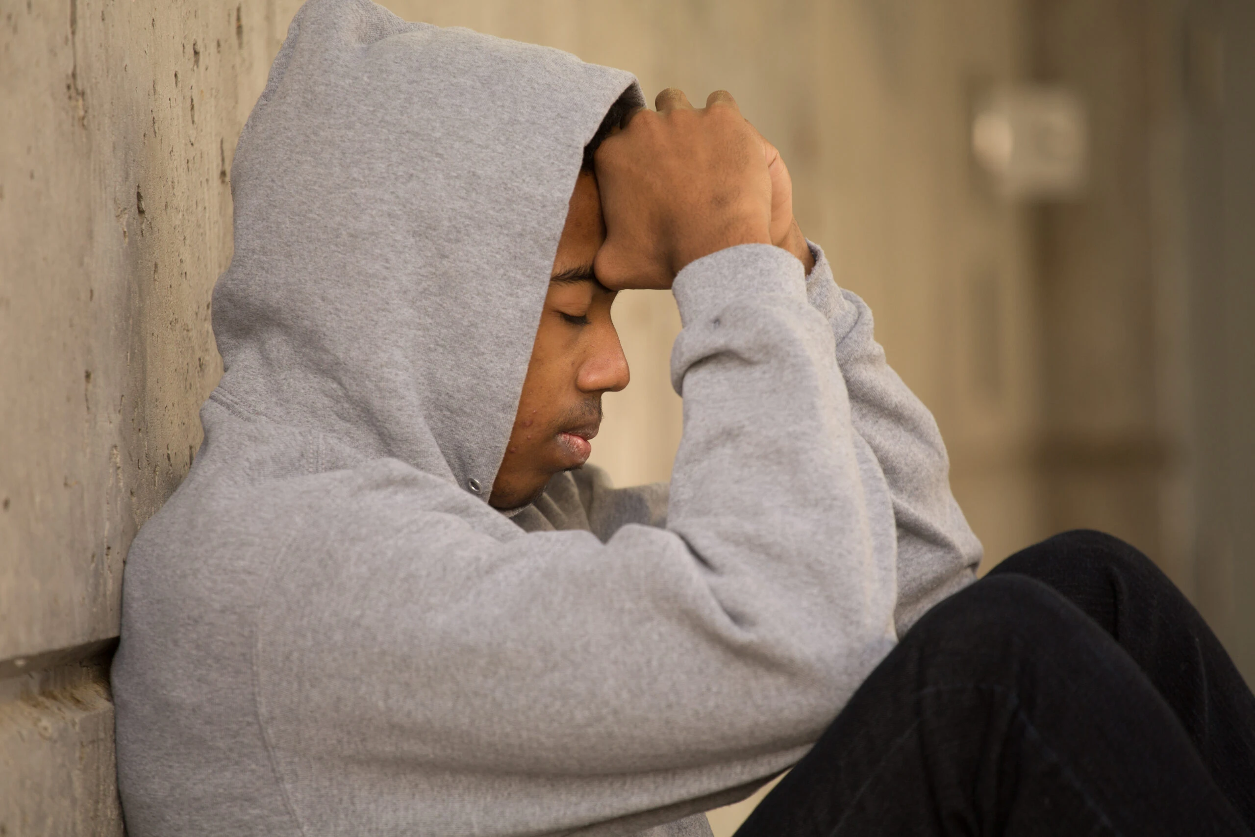 young person sitting against wall with their head in their hands